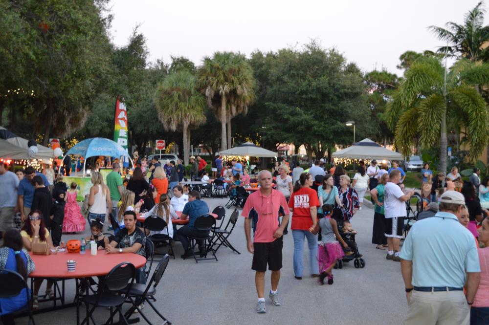 People walk through area and sit at tables in street near vendors